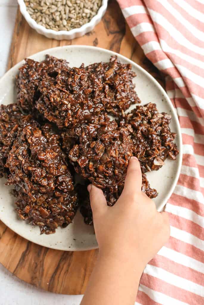 a little hand reaching for a paleo no bake cookie from a plate 