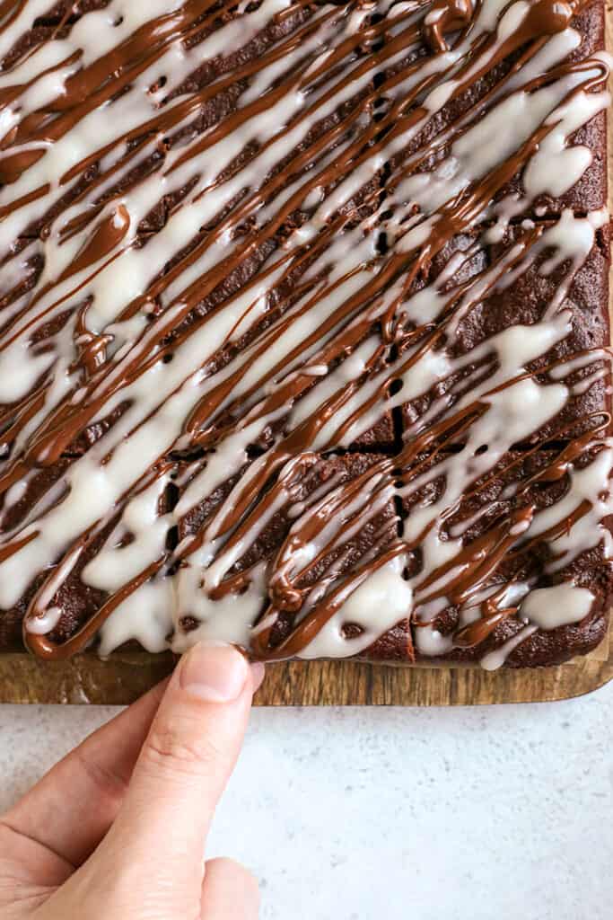 a hand reaching for a paleo peppermint glazed brownie 