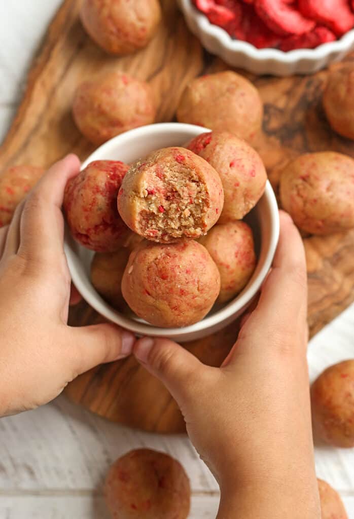 paleo vegan strawberry shortcake bites in a bowl with little hands holding it