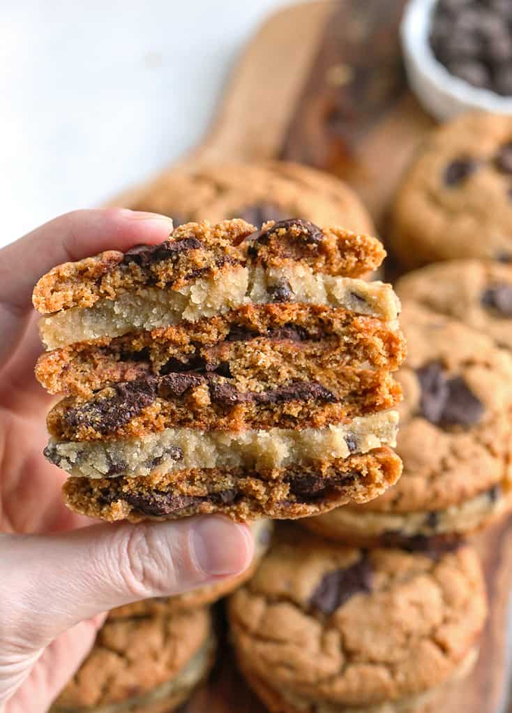 hand holding stacked paleo chocolate chip cookie dough sandwiches with the inside showing 