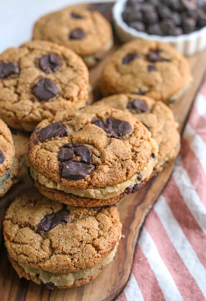 cutting board with a pile of paleo chocolate chip cookie dough sandwiches 