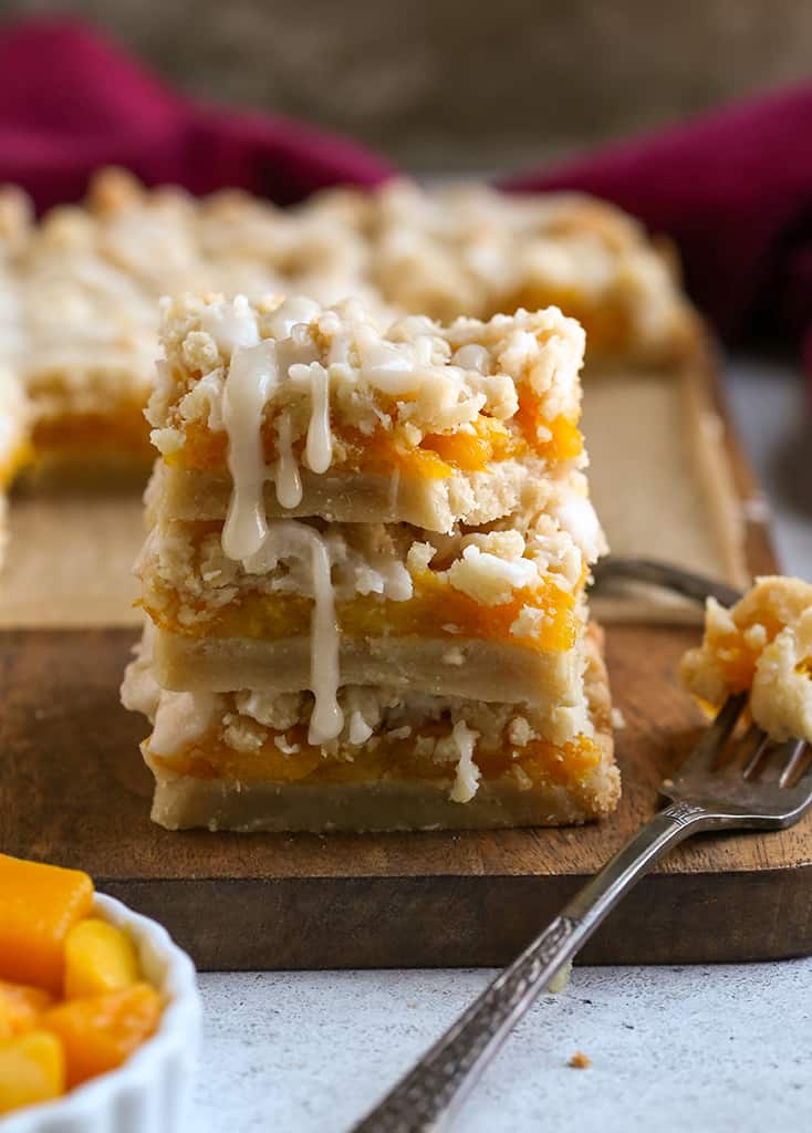 stack of paleo vegan mango crumb bars with a bite taken out of the top one, glaze dripping down