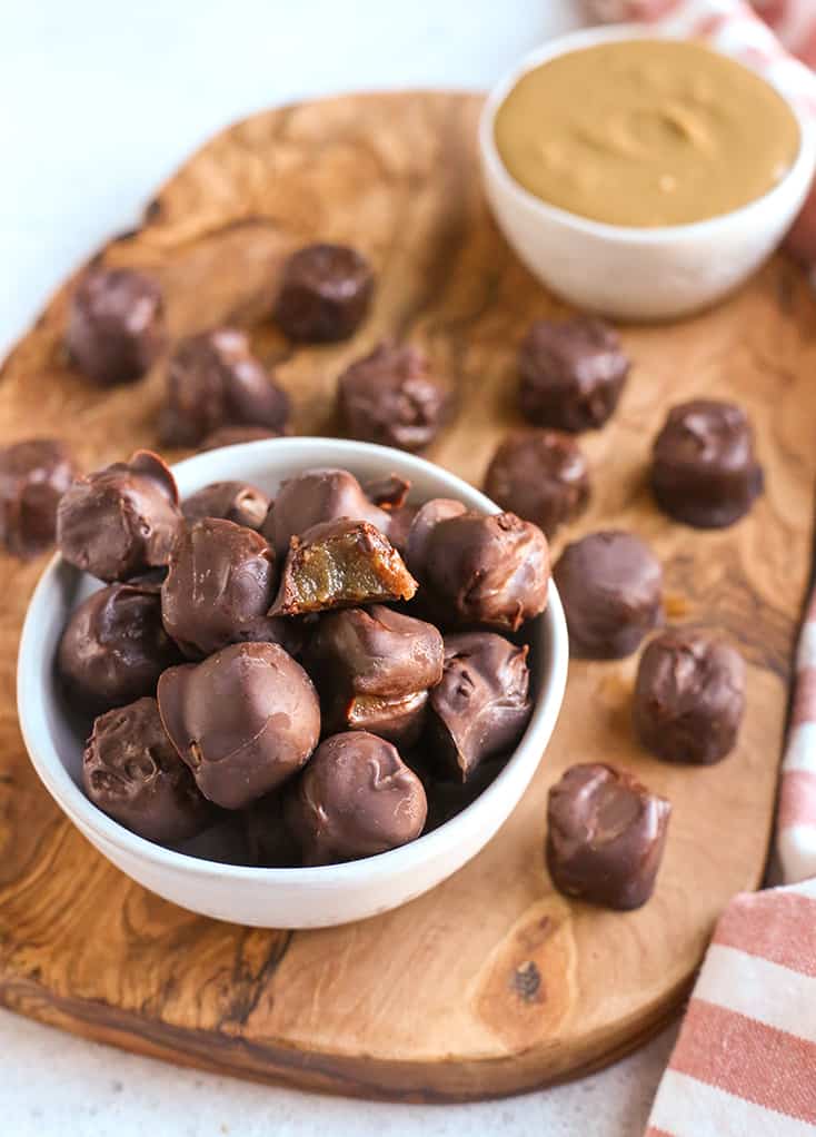 bowl of paleo vegan rolos with a bite taken out of one and the caramel showing 