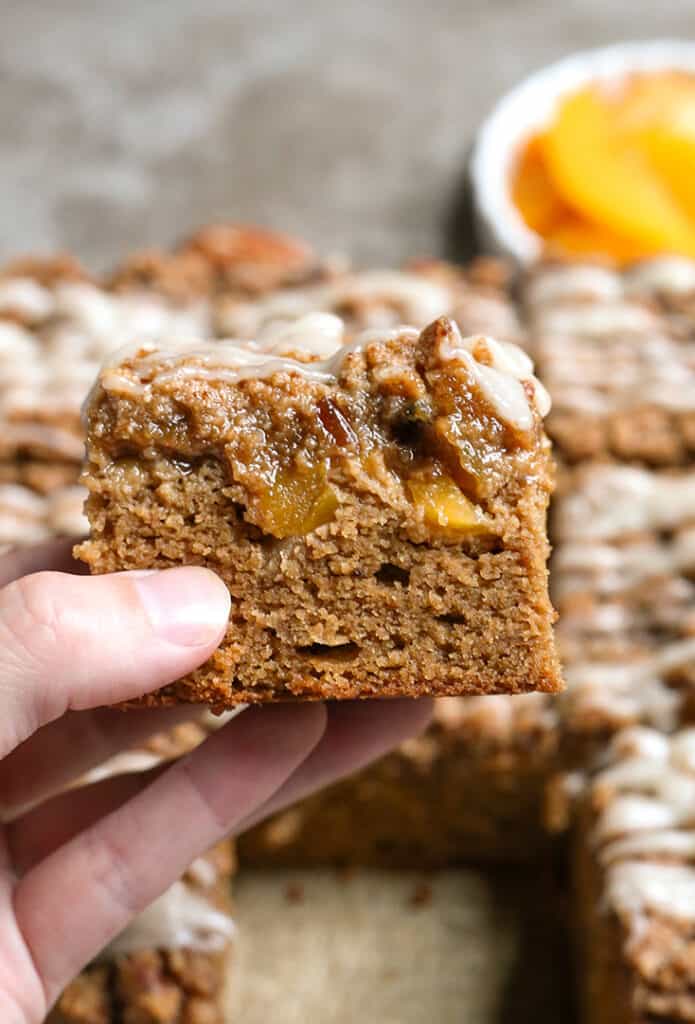 a hand holding a piece of paleo peach coffee cake