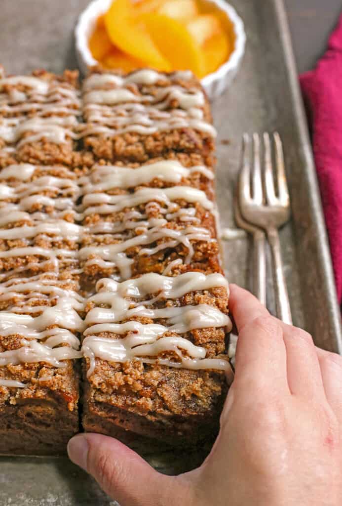 hand grabbing a piece of paleo peach coffee cake 