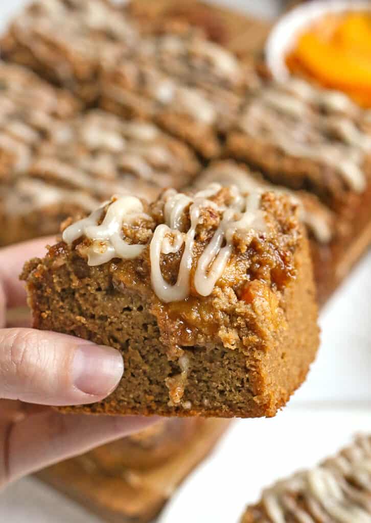 a hand holding a piece of peach cobbler coffee cake with glaze on top