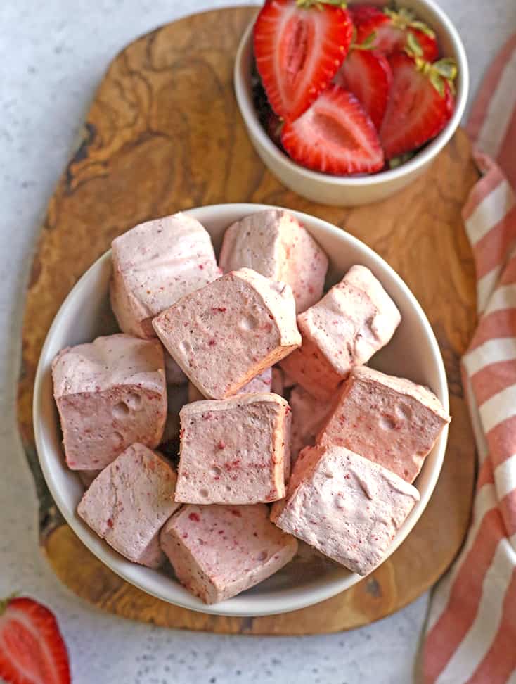 a bowl of strawberry marshmallows on a wooden cutting board 