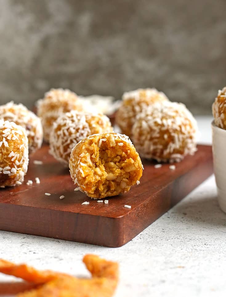paleo vegan mango coconut bites sitting on a cutting board, one with a bite taken out