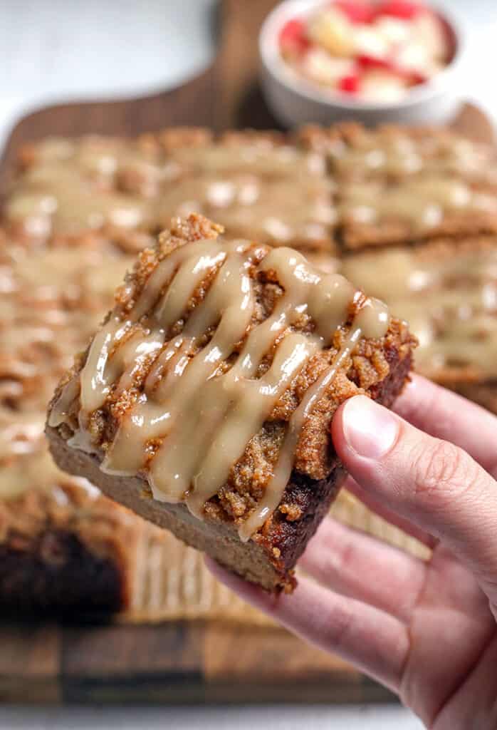 hand holding a piece of apple coffee cake with the top showing which has a drizzle on it 