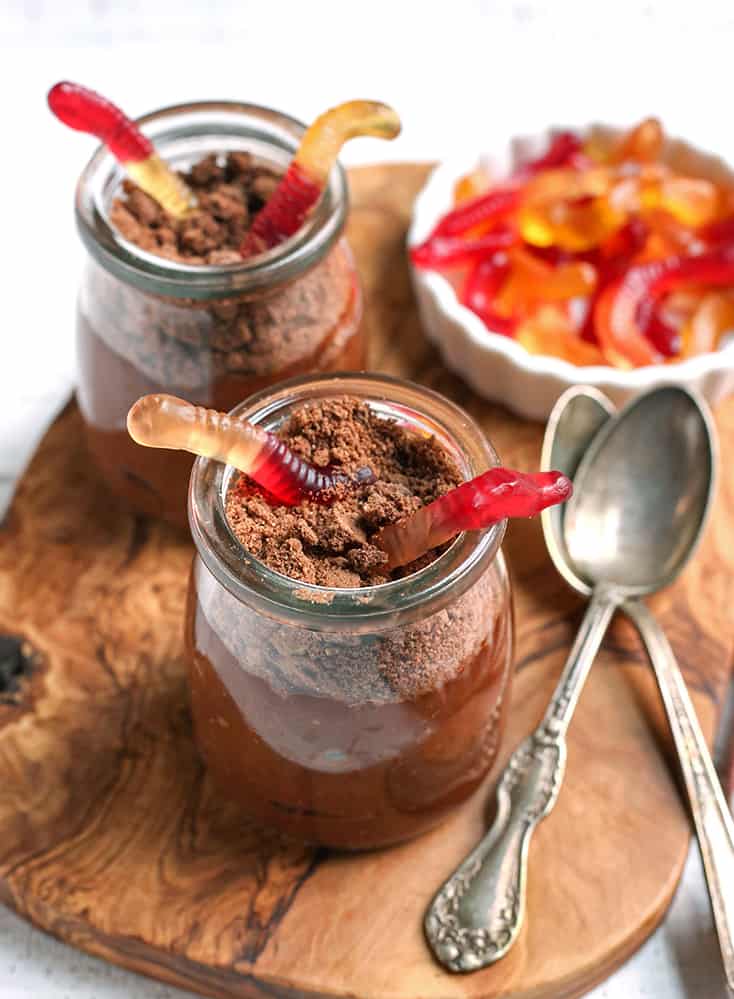 a cutting board with two paleo dirt pudding cups on it with spoons next to them 