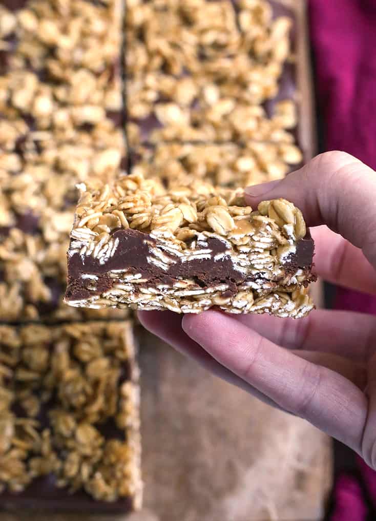 a hand holding a gluten free oatmeal chocolate fudge bar, showing the layers
