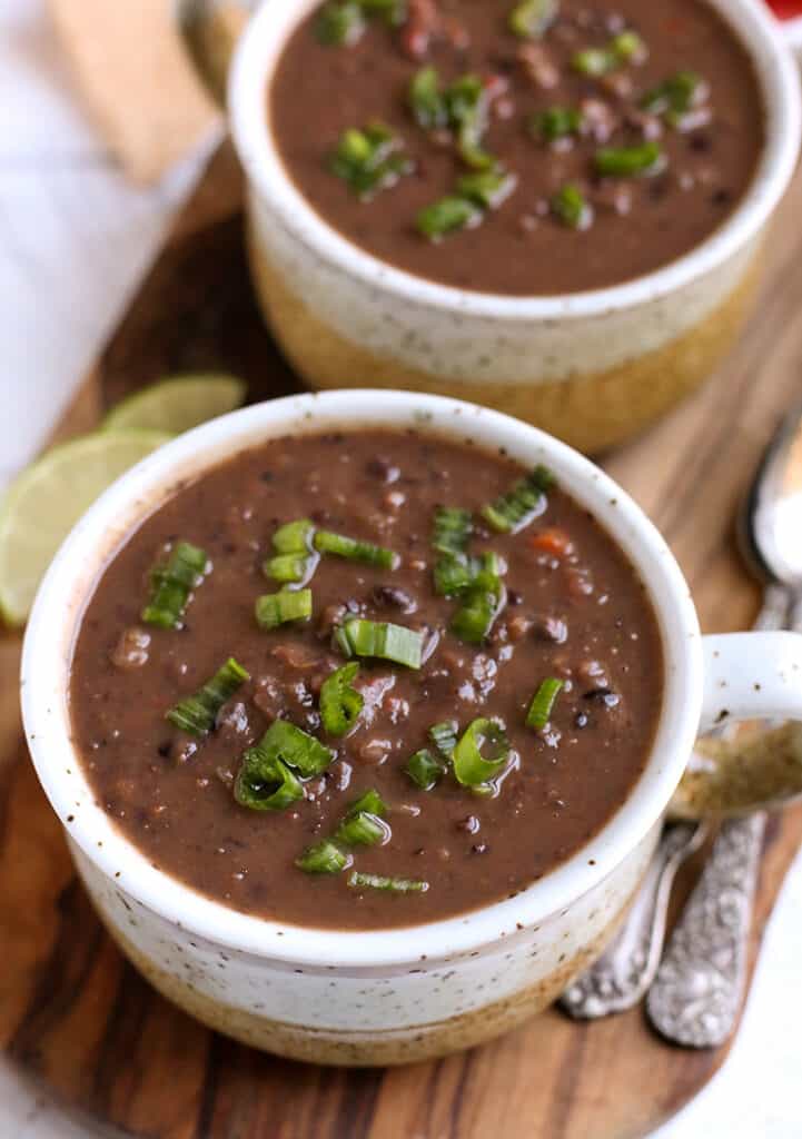 two bowls of vegan black bean soup on a wooden cutting board 