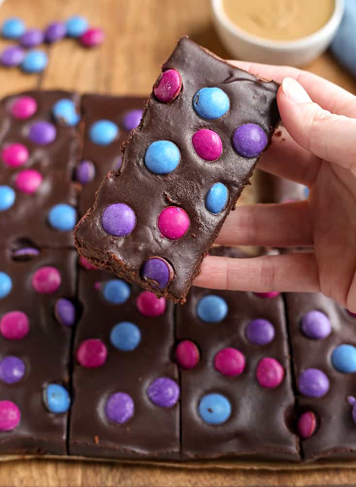 a hand holding a brownie with candies on top, the top showing 
