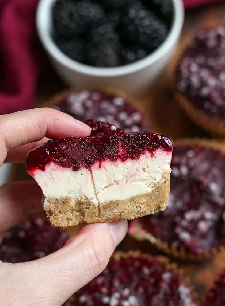 hand holding a gf blackberry cheesecake that is cut in half with the middle showing 