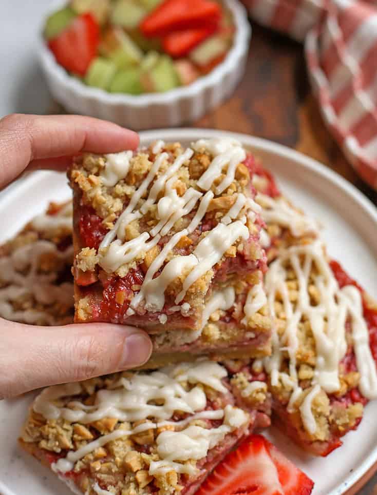 hand reaching for a strawberry rhubarb bar on a plate 