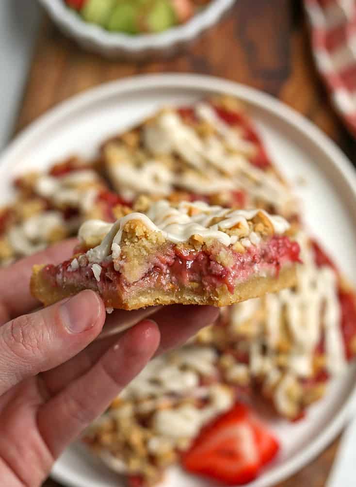 hand holding a strawberry rhubarb bar with a bite taken out of it 