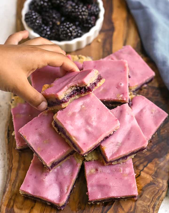 small hand reaching for a blackberry pop tart bar on a stack of them