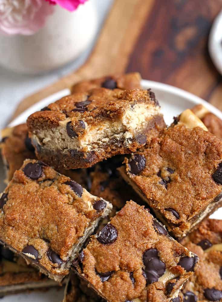a plate of grain free chocolate chip cookie cheesecake bars with a bite taken out of the top one 