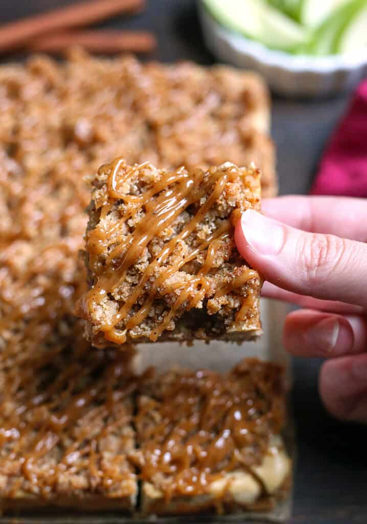 hand holding a gluten free caramel apple cheesecake bar, showing the top with caramel drizzle 