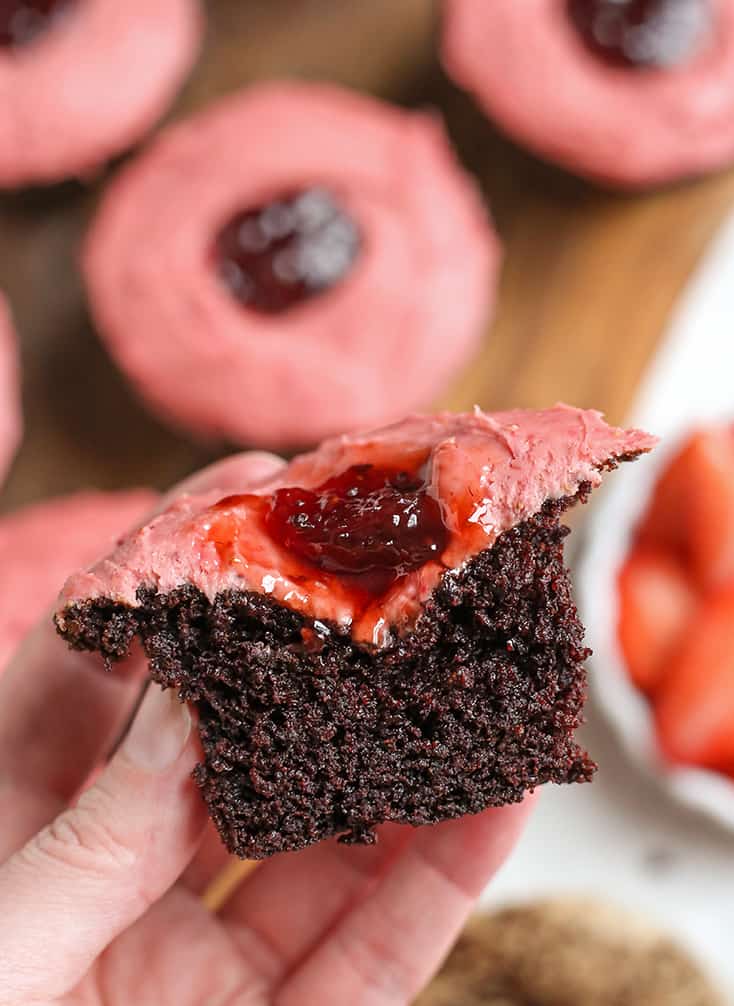 hand holding a chocolate cupcake with strawberry frosting with the middle showing
