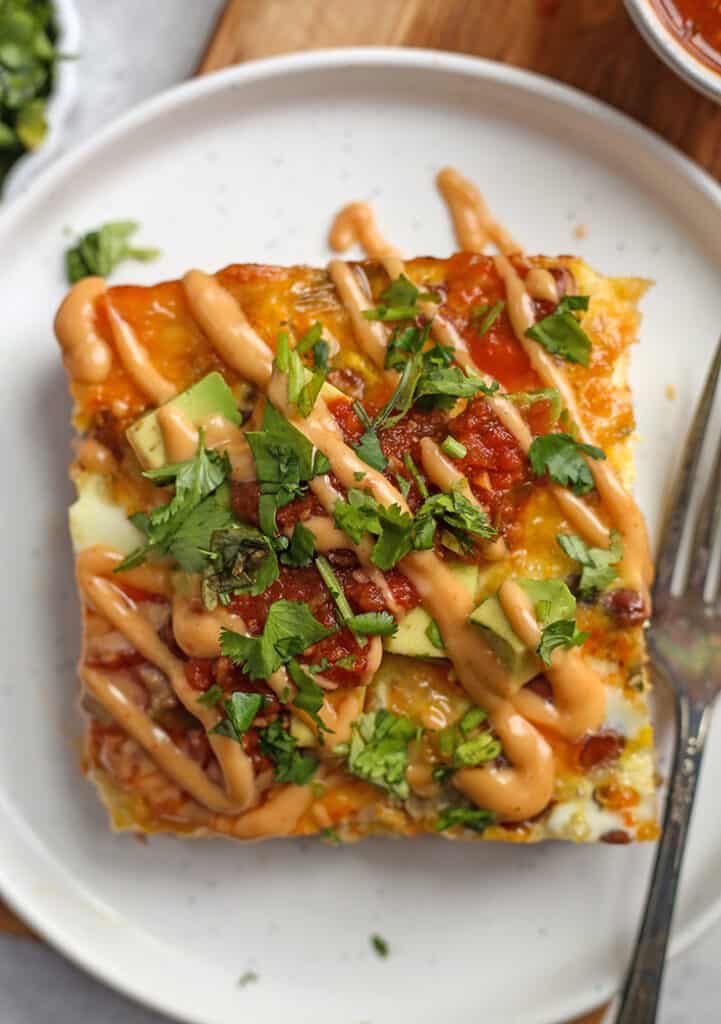 a piece of Mexican style breakfast casserole on a plate with avocado, salsa and cilantro on top 