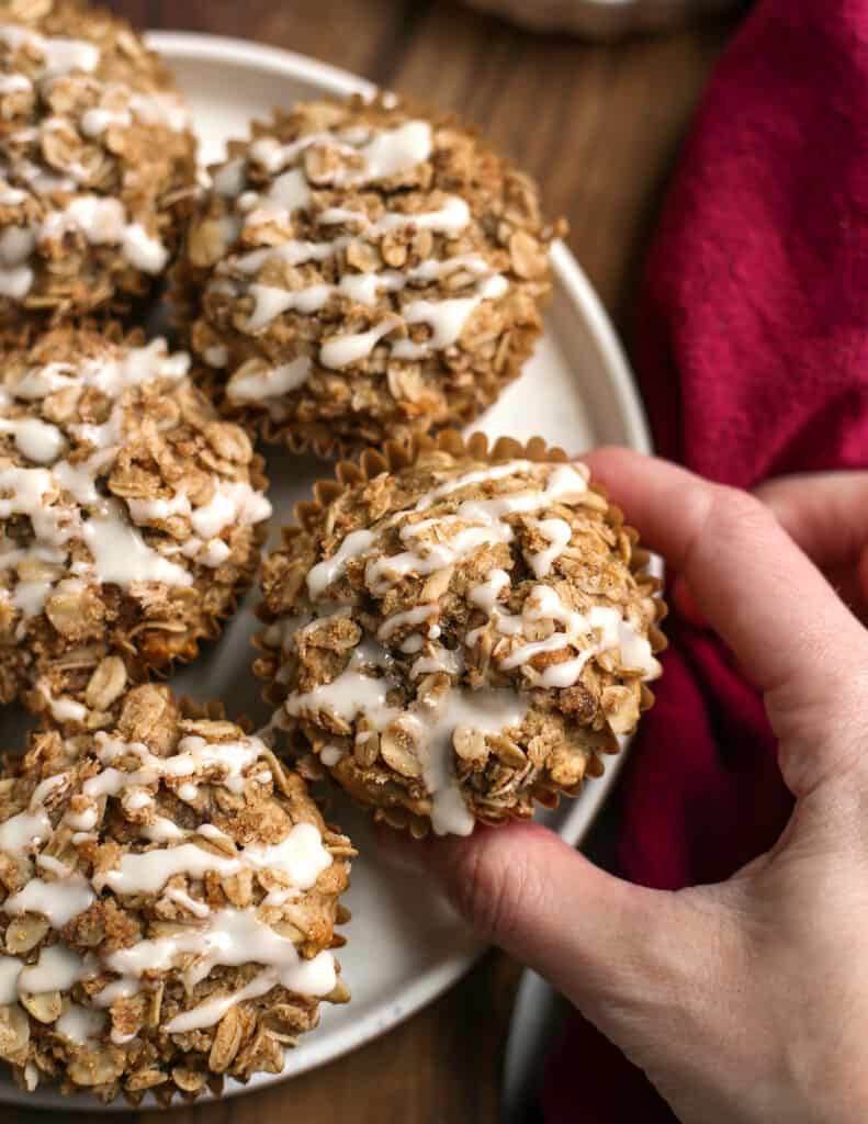 hand reaching for a banana muffins off a plate with more muffins on it. 