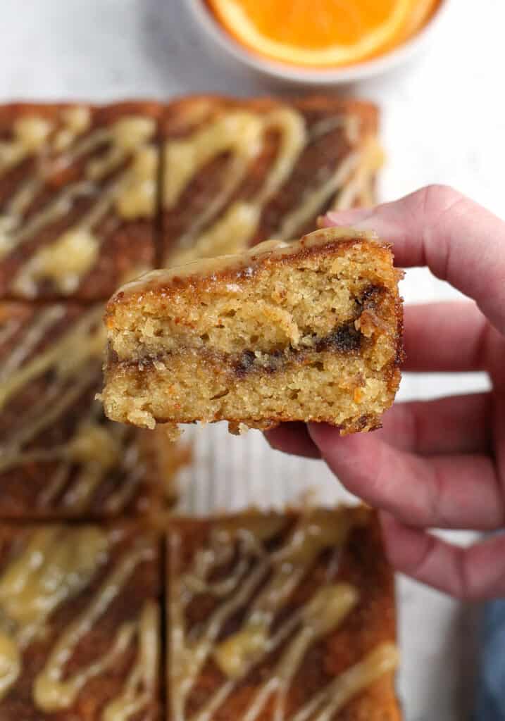 a hand holding a piece of orange cinnamon coffee cake showing the cinnamon swirl on the inside. 