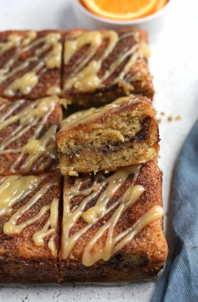 orange cinnamon coffee cake on a cutting board with one piece propped up showing the cinnamon swirl on the inside. 