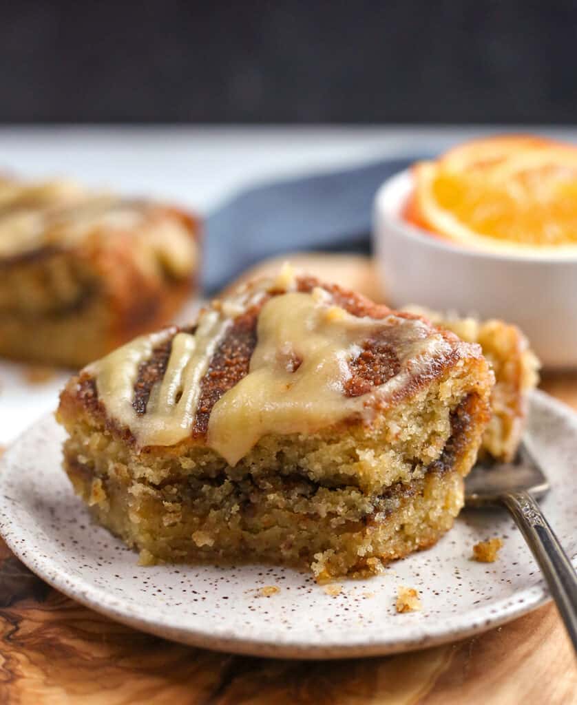 a piece of paleo orange coffee cake on a small plate with a bite taken out of it and a fork next to it. 