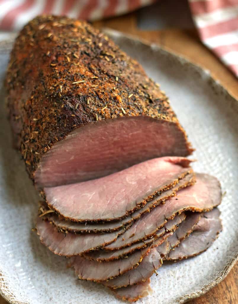 roast beef of a platter with think slices cut from it showing the middle 