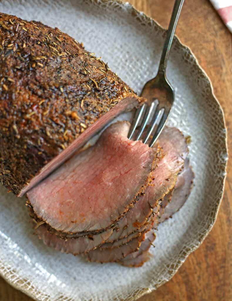 top view of sliced roast beef on a platter with a fork in the top piece 