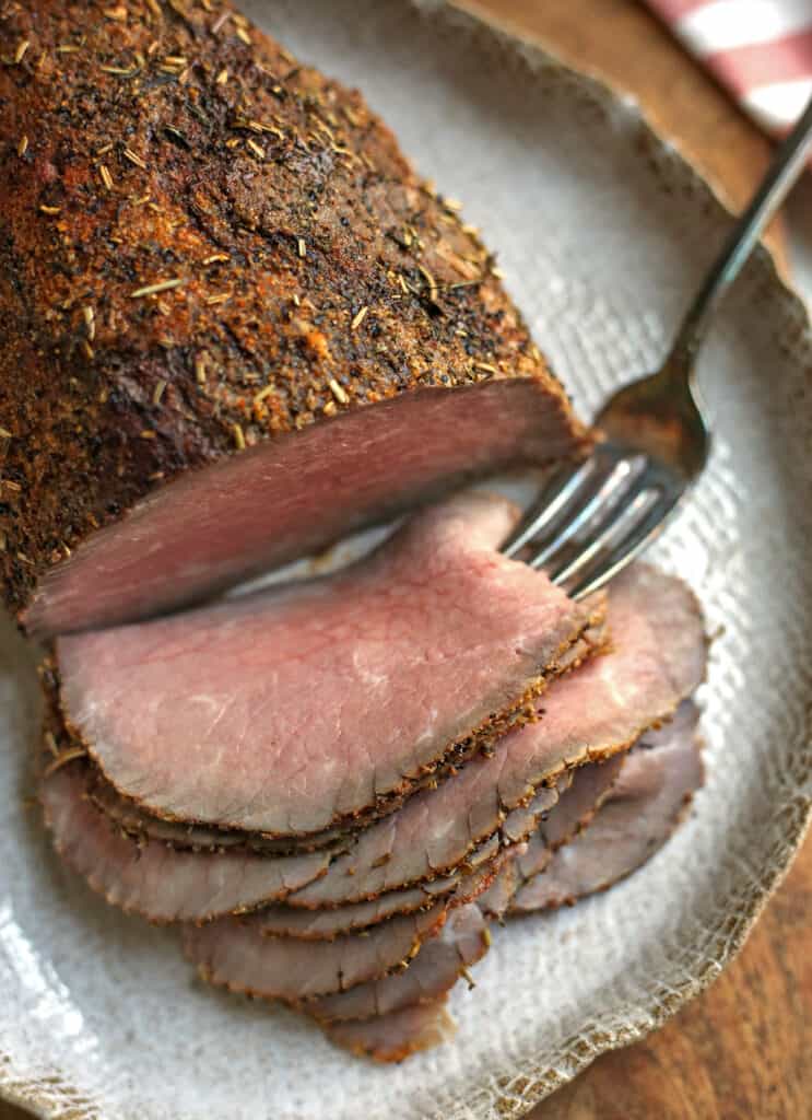 roast beef on a platter with slices cut and a fork in the top slice. 