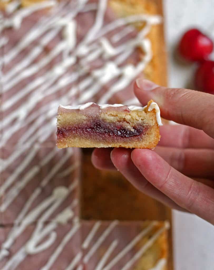 a hand holding a cherry pop tart bar showing the cherry filling. 