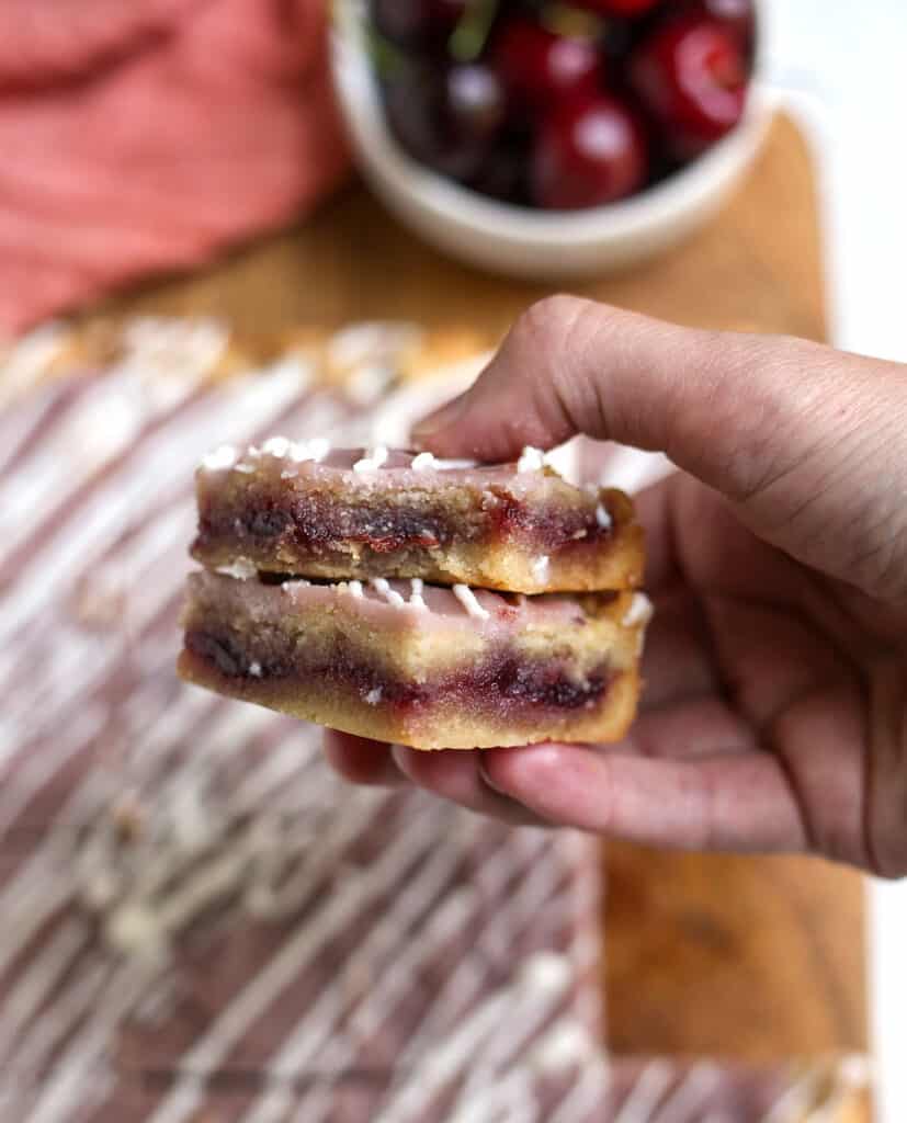 a hand holding two berry pop tart bars stacked. A bite taken out of the top one and the cherry filling showing. 