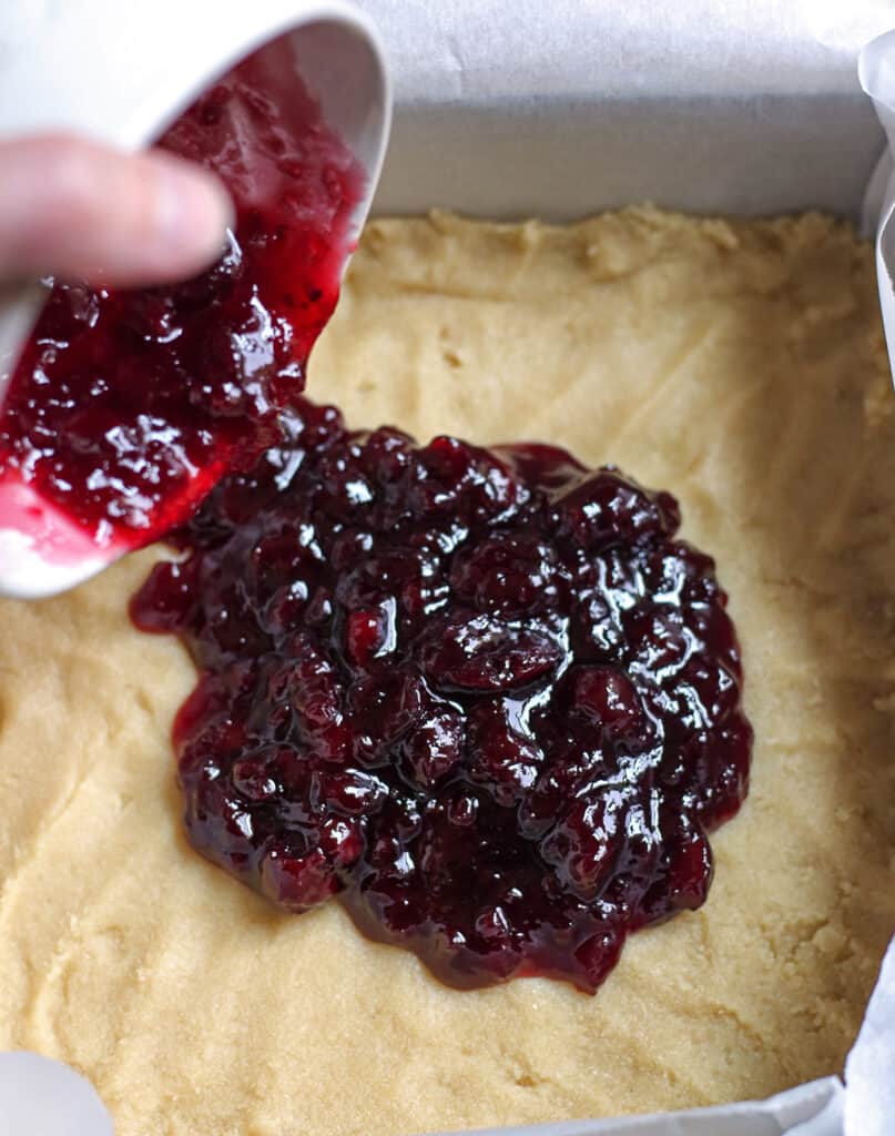 cherry preserves being poured over the shortbread crust. 