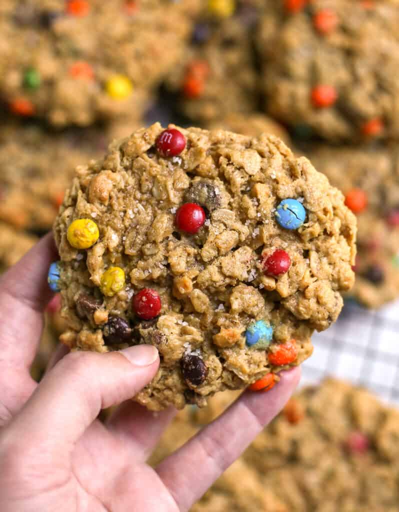 hand holding a big monster cookie with more in the background. 