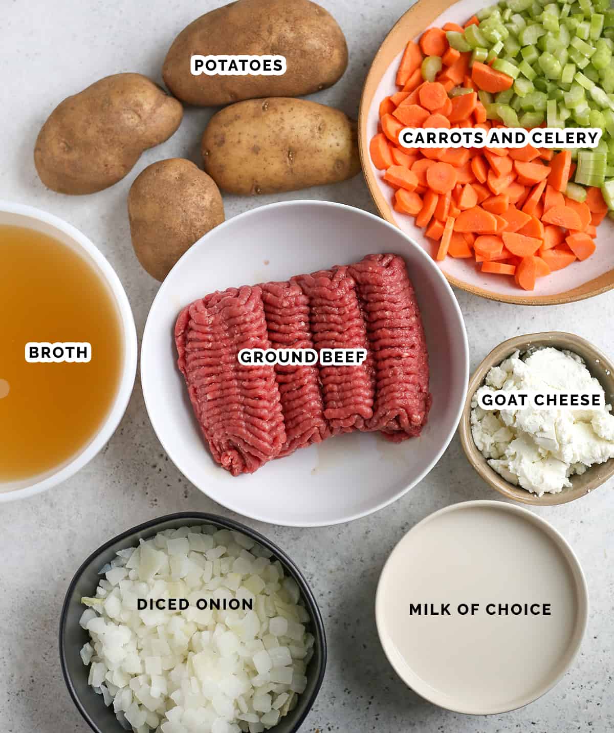 All the ingredients of cheeseburger soup in individual bowls- ground beef, broth, onion, milk, got cheese, carrots, celery and potatoes.  
