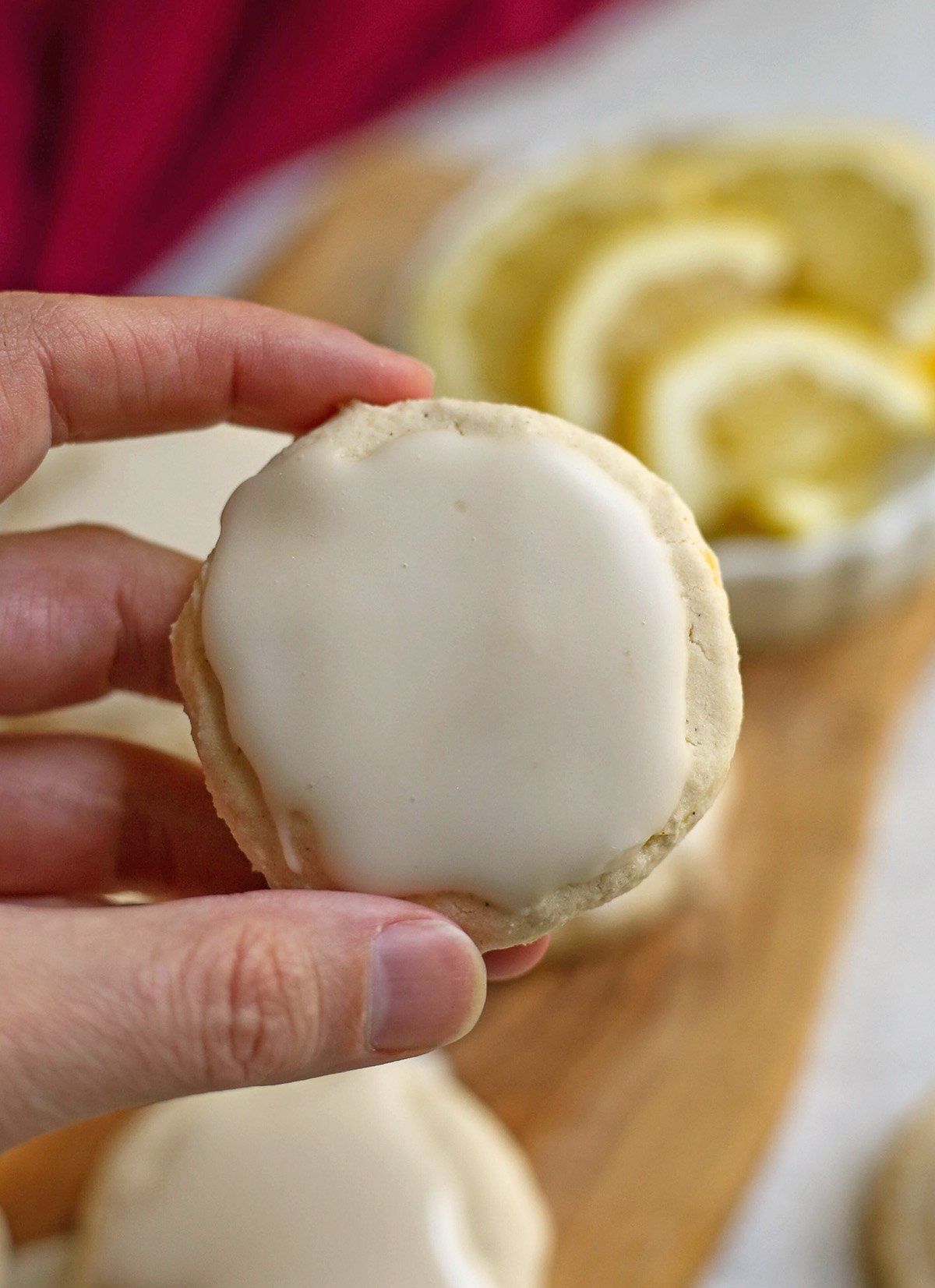 A hand holding a lemon cookie showing the frosting on top.