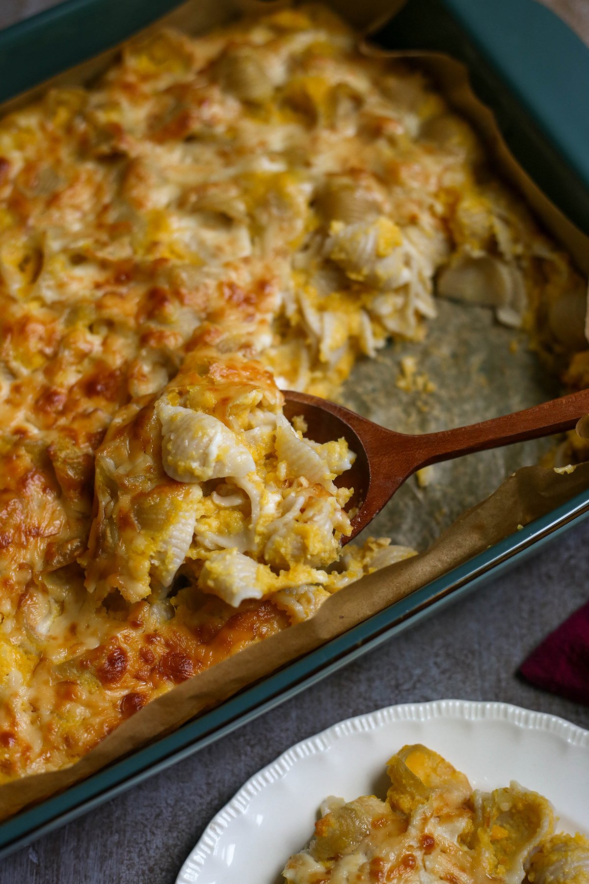 Mac and cheese baked in a pan with a spoon taking a serving out of it.