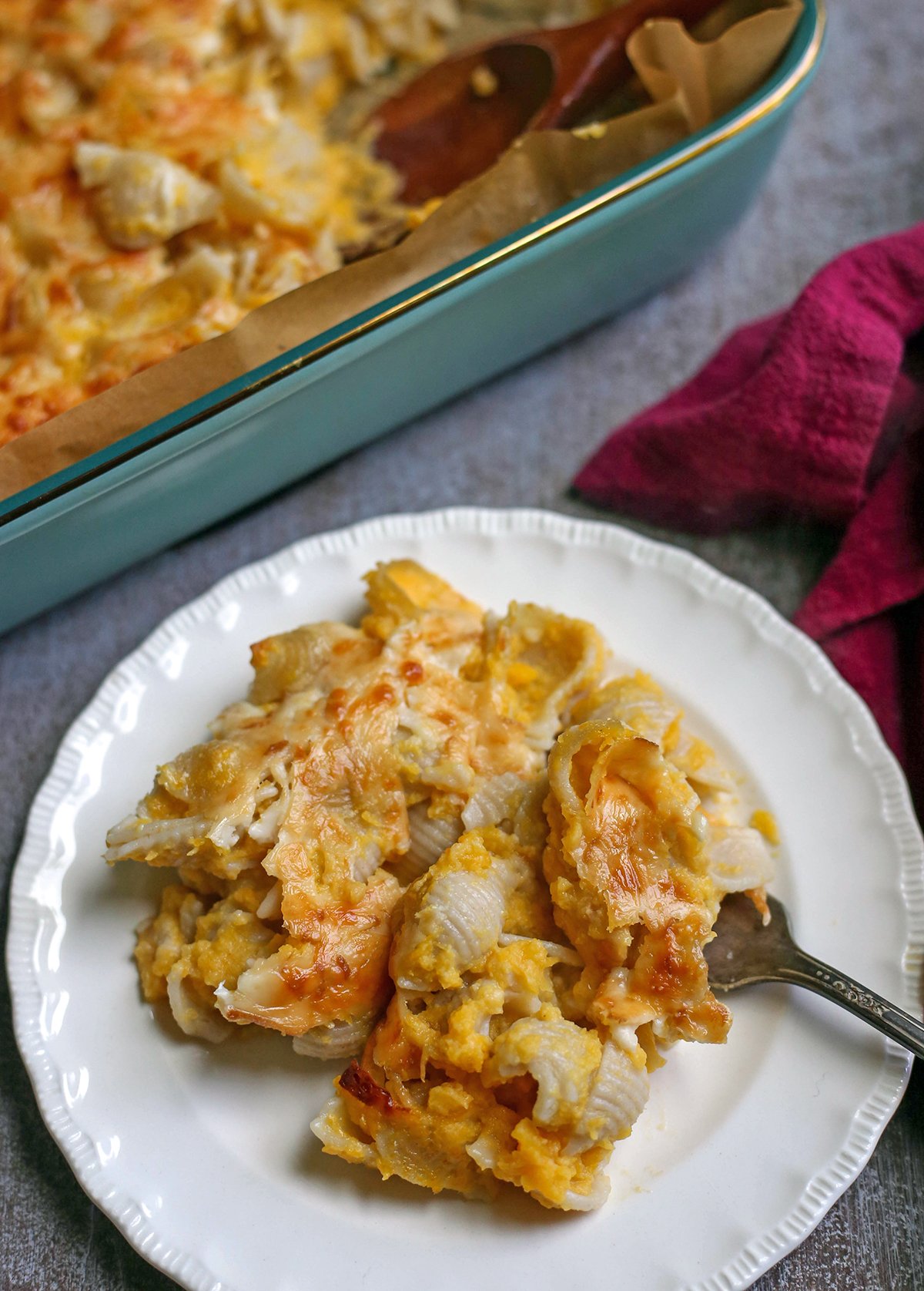 A small white plate with butternut squash Mac and cheese on it with a fork in the pasta.